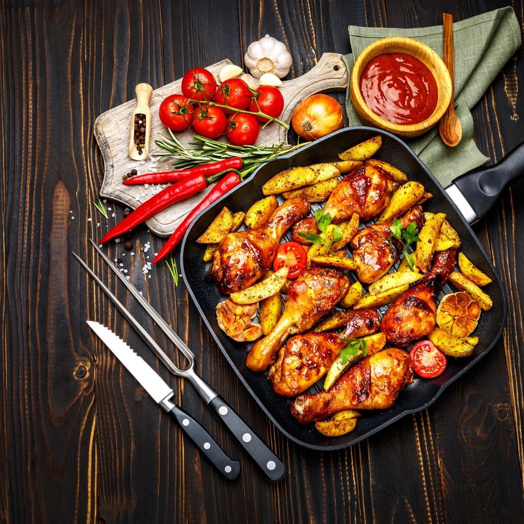 Paprika-roasted chicken drumsticks and golden potato wedges with roasted garlic in a tray